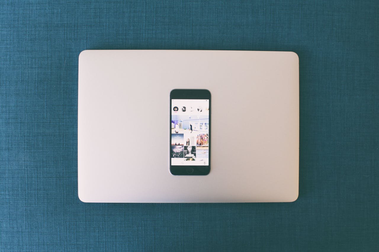 Flat lay of a smartphone on a laptop with social media photos on screen.